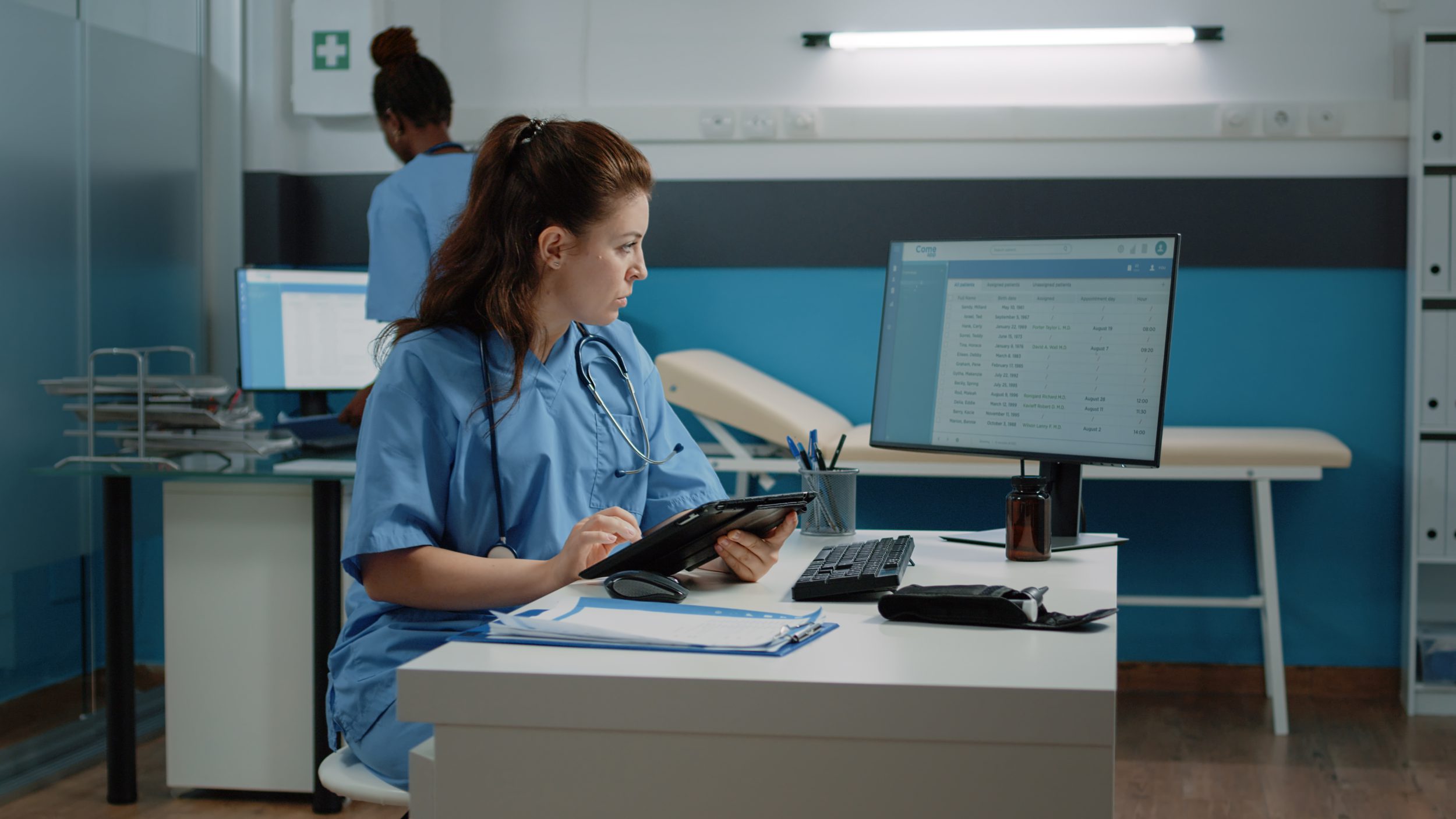 Nurse charting and looking at monitor while using modern gadget for healthcare checkup visit.