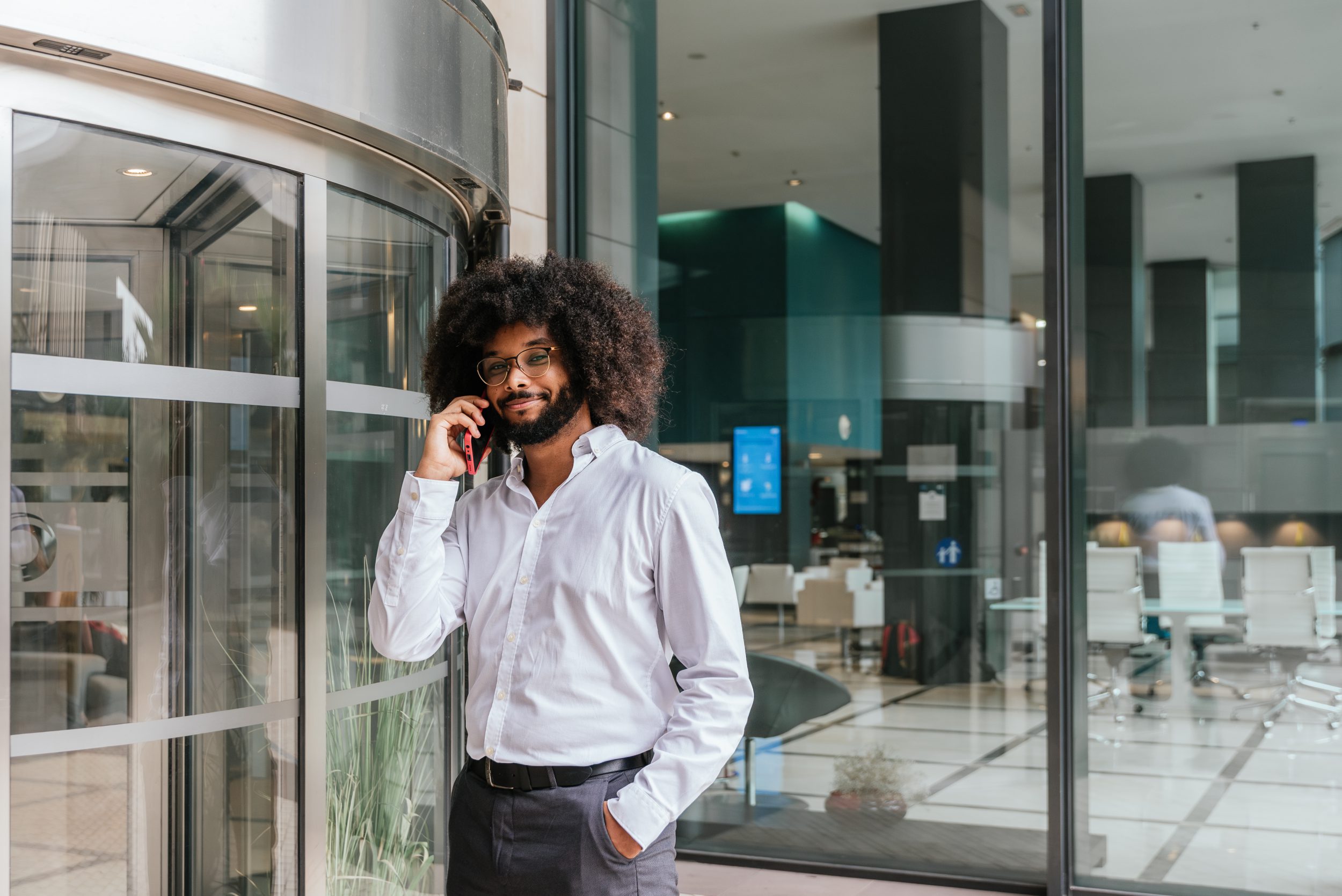 portrait of young afro businessman standing at the entrance of a smart building talking by mobile phone