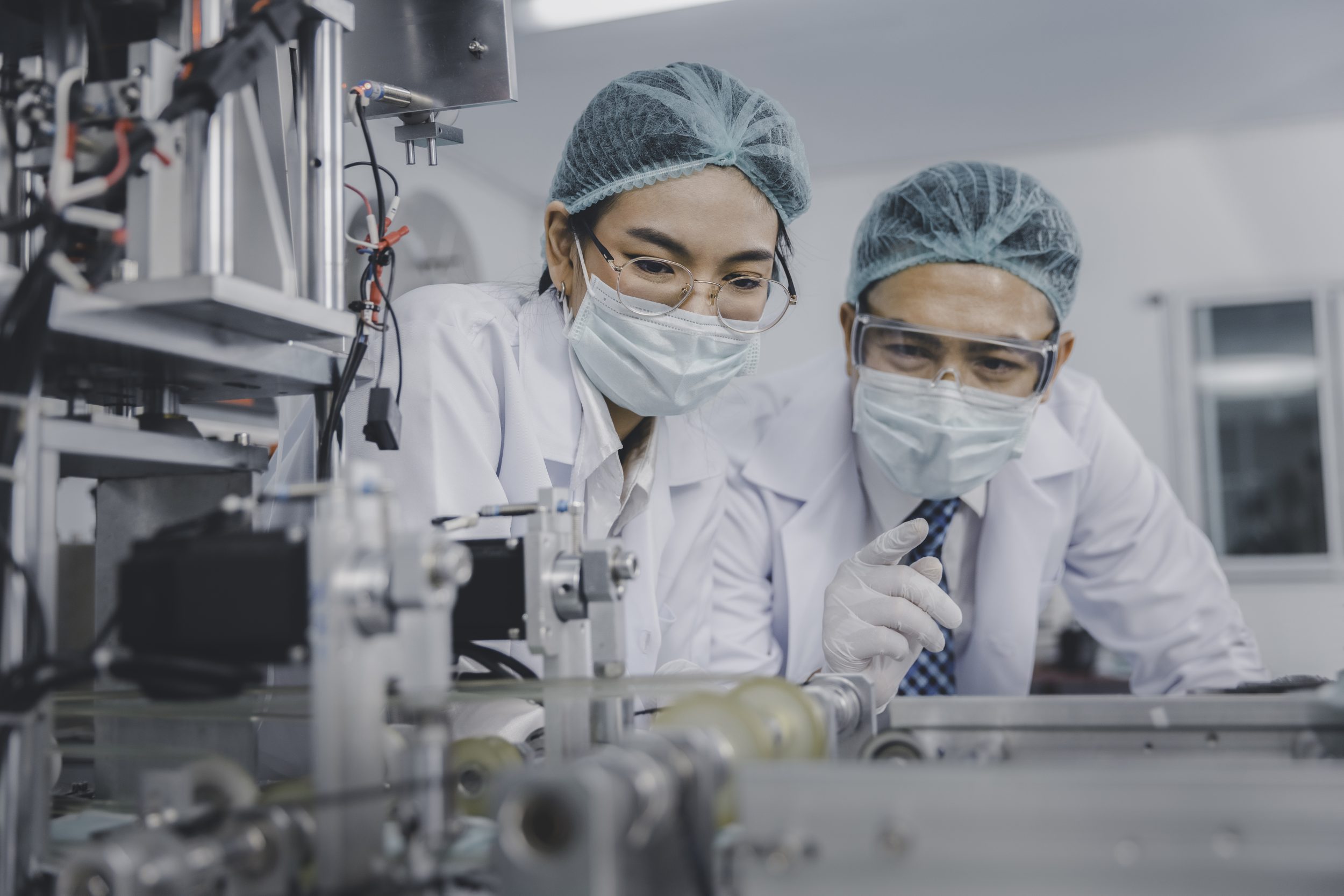 Two Asian doctor or engineer working at clean medical mask production factory as part of Medical Equipment Manufacturer OEM